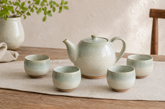 Ivory and celadon ceramic teapot with matching cups on a linen runner
